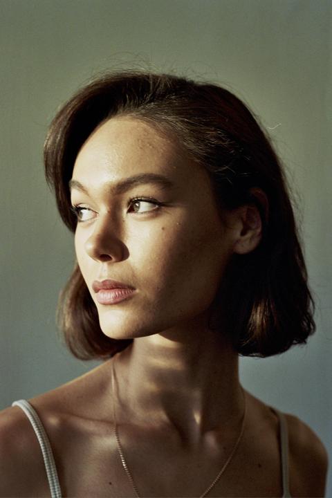 A woman with short brown hair looks to the right, with light falling on her face and shoulder.