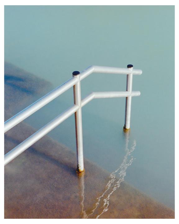 A metal handrail extends into light blue water with steps visible beneath the surface.
