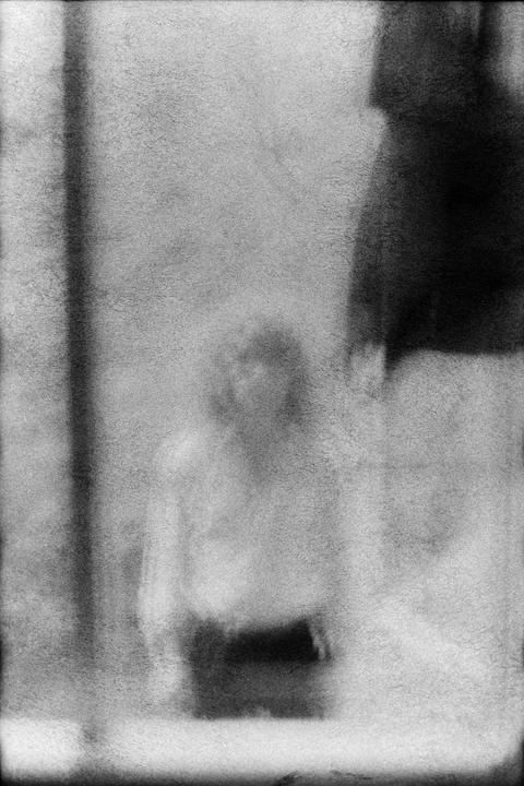 A blurry figure of a person is visible through a textured surface, with dark shapes on the right and left.
