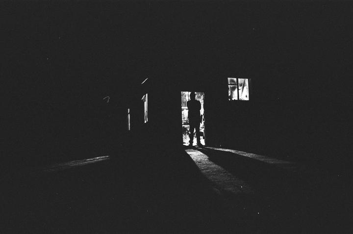 A man stands silhouetted in a doorway with light streaming in from behind him and a window to his right.