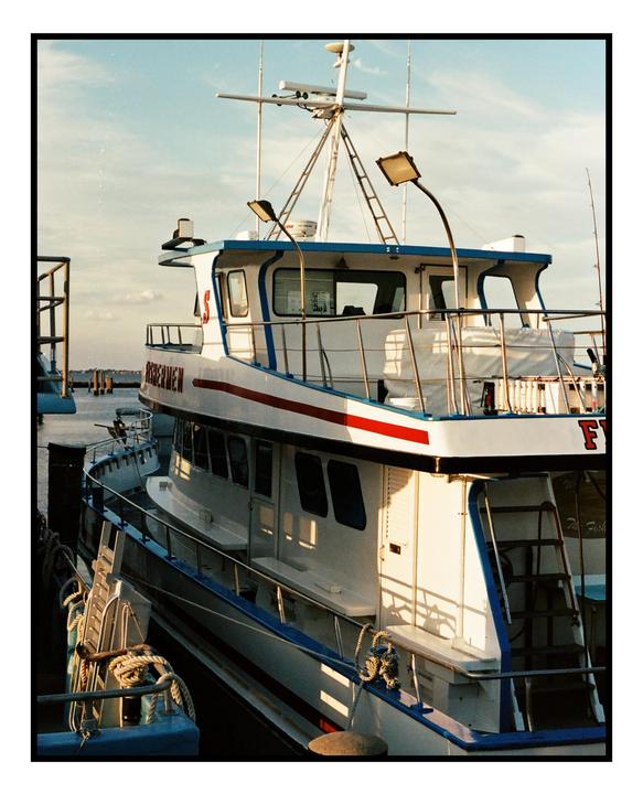 A white and blue boat with red trim is docked at a harbor under a clear sky.