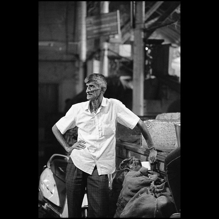 A man in a white shirt stands with his hands on his hips next to a scooter and sacks.