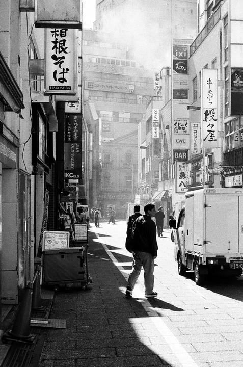 A man walks down a narrow street lined with buildings and signs in a city.