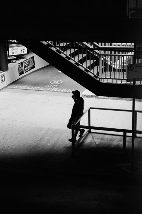 A man stands in shadow under a staircase next to a "no pedestrian" sign on the ground.