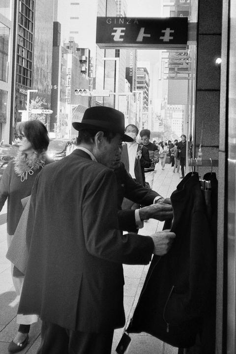 A man in a hat and suit looks at clothing hanging outside a store on a city street.