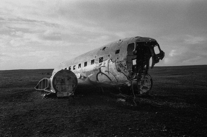 A crashed airplane fuselage with graffiti on its side rests on a barren landscape under a cloudy sky.