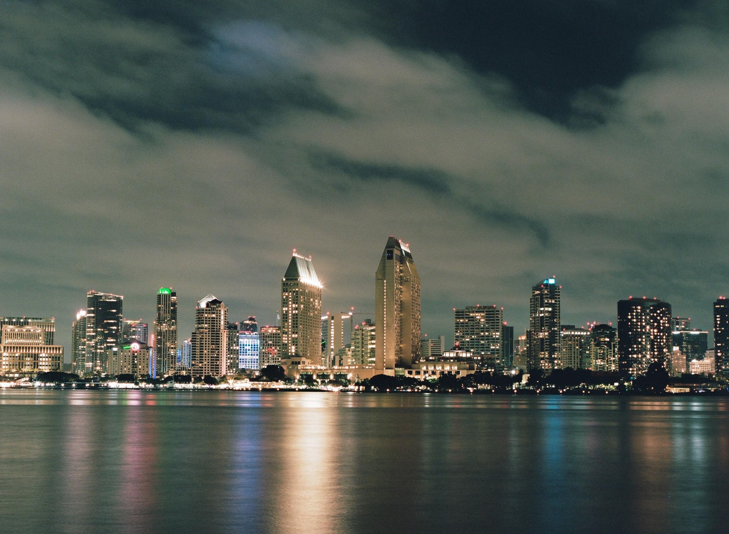 The San Diego skyline is visible at night across a body of water with reflections of the city lights.