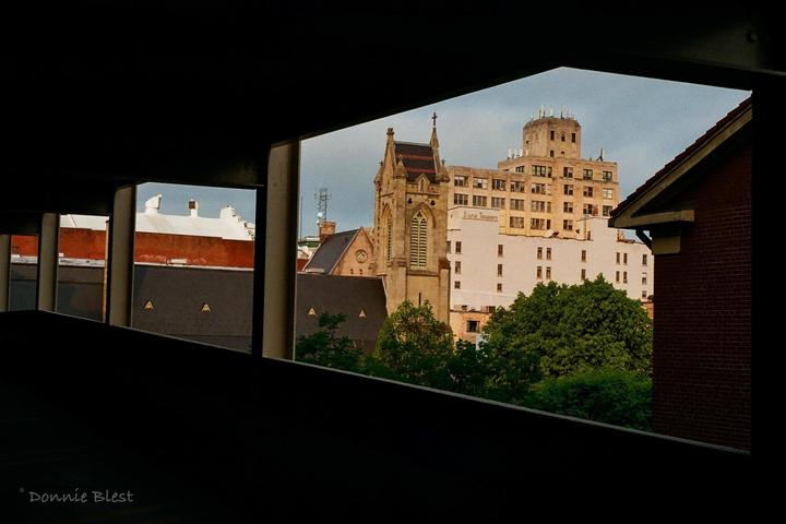 A church steeple and a tall building are visible through the dark, rectangular openings of a structure.