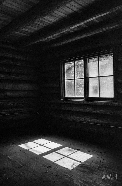 Sunlight streams through a window, casting a grid of light onto the floor of a dark, rustic room.
