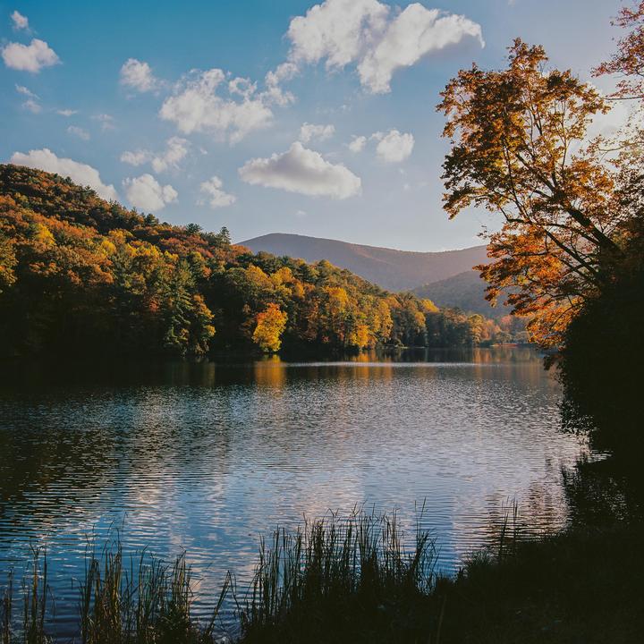 A lake is surrounded by hills covered in autumn foliage under a blue sky with clouds.