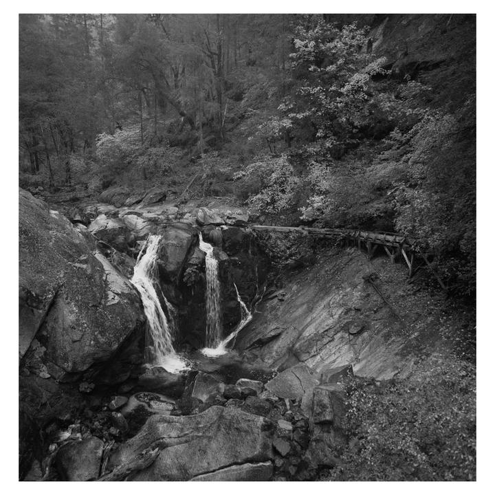 A waterfall cascades over rocks in a forest with a wooden structure built into the hillside.