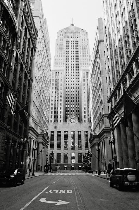 A street is lined with tall buildings and flags, with a large building at the end of the street.