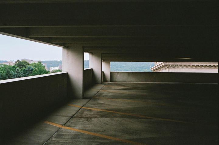 A parking garage with yellow lines on the ground looks out onto a city with trees and buildings.