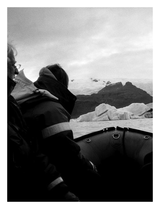 Two people in a boat look out at a glacial landscape with icebergs on the water.