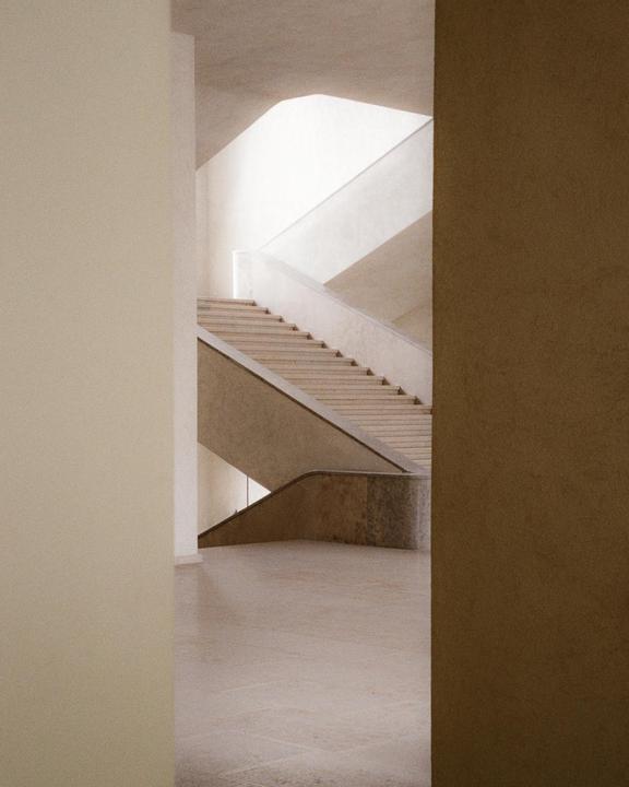 A minimalist architectural interior features a light-colored staircase with a curved railing, illuminated by natural light from above.