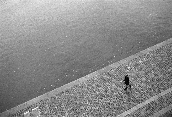 A person walks along a cobblestone path next to a body of water.