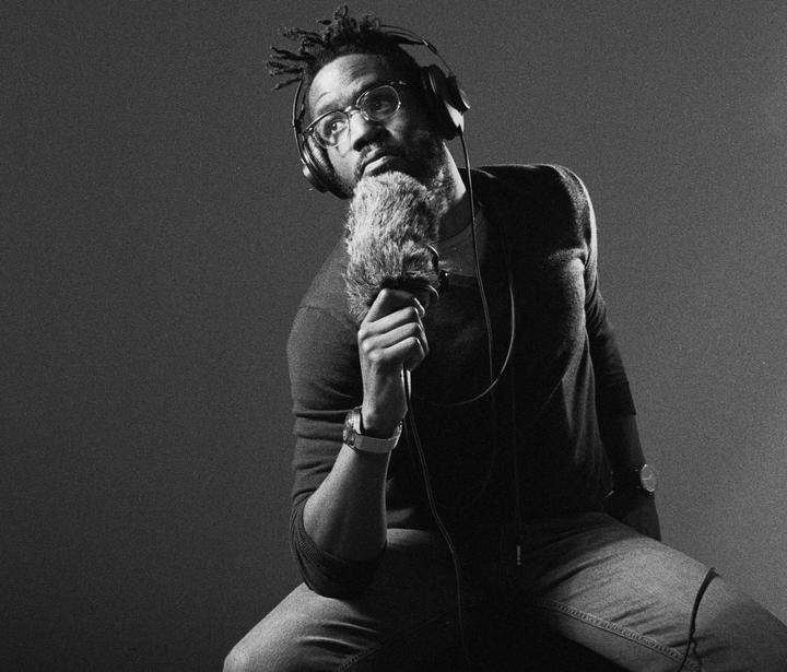 A man wearing headphones and glasses holds a furry microphone and looks up.