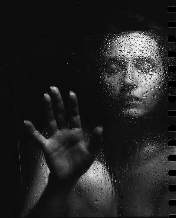 A person's face and hand are visible through a wet, dark surface.