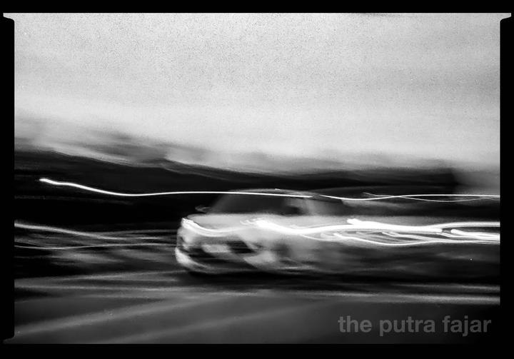A blurred car with light trails is captured in motion against a dark background.