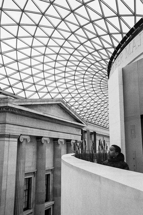 A boy stands on a balcony overlooking a large hall with a glass-domed ceiling and classical architecture.
