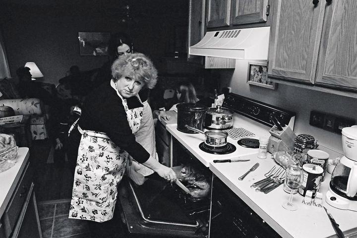 A woman wearing an apron is taking a turkey out of an oven in a kitchen.