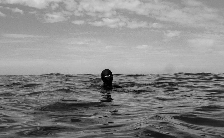 A person wearing a balaclava is swimming in the ocean under a cloudy sky.