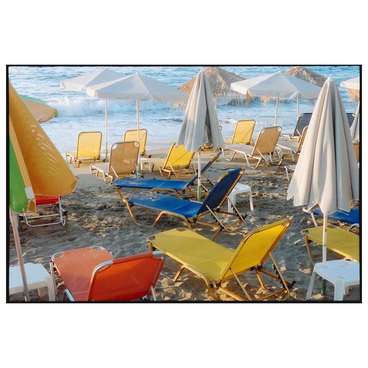 Colorful beach chairs and umbrellas are scattered across a sandy beach with waves crashing in the background.