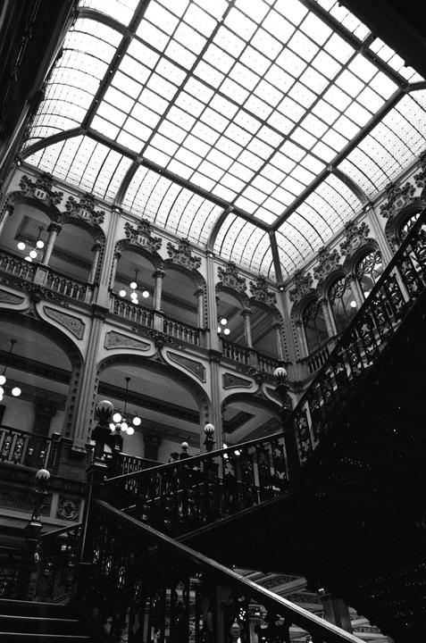 A grand interior with multiple levels of ornate balconies and a large glass ceiling is captured from a low angle.
