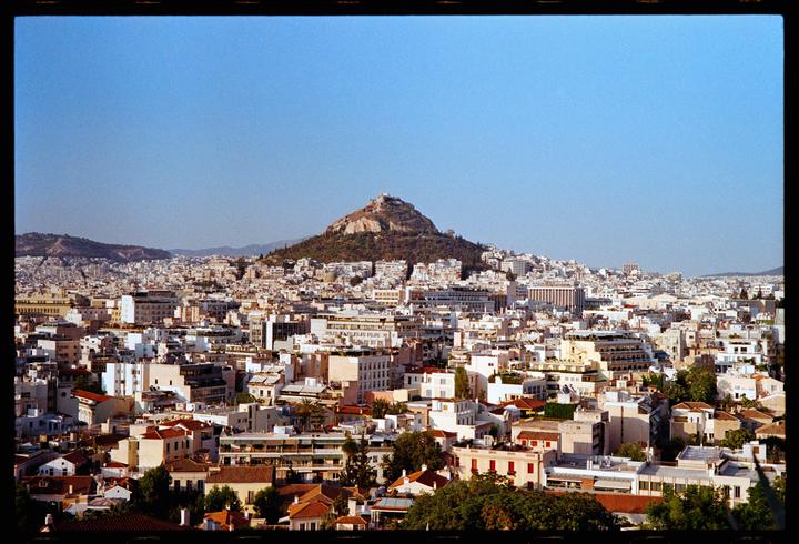 A panoramic view of Athens shows a city with many buildings and a large hill in the distance.