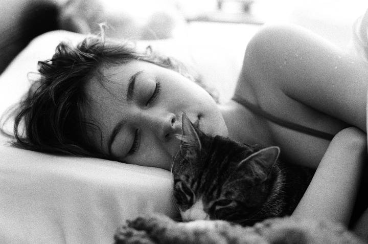 A woman and a cat are sleeping together in a bed.