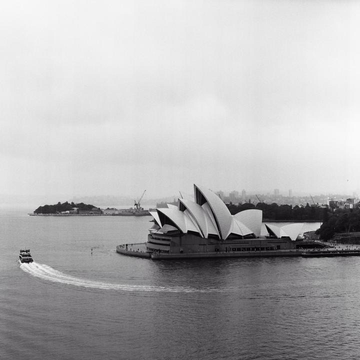 A boat leaves a wake as it passes the Sydney Opera House on a cloudy day.