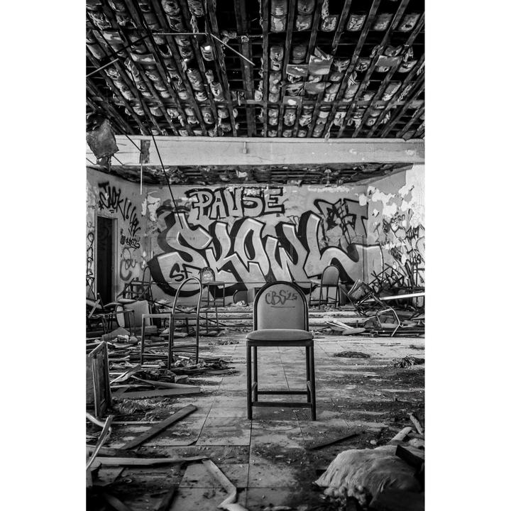 A single chair stands in the middle of a derelict room covered in graffiti and debris.