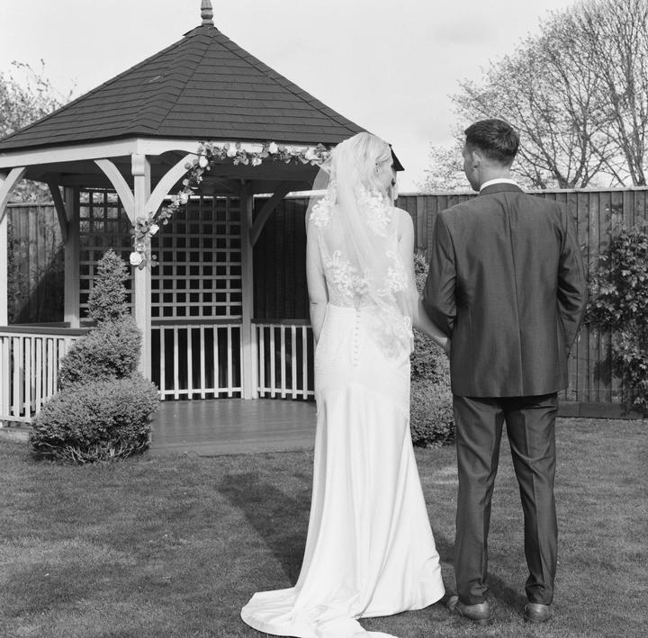 A couple stands in a garden looking at a gazebo.