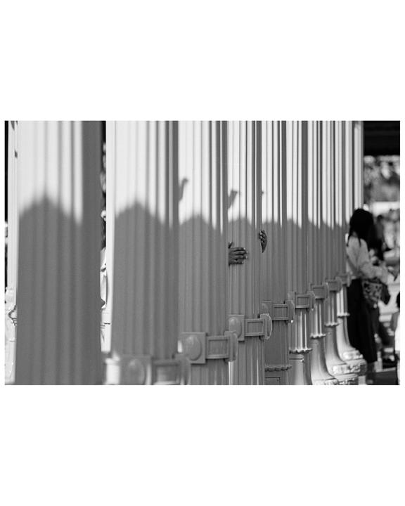 A person's hands are visible between two columns, with shadows of other hands on the column.