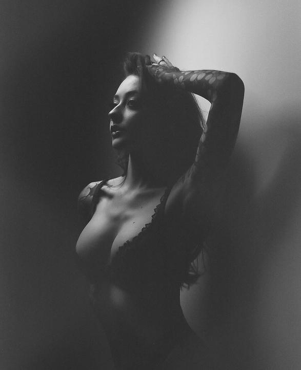A woman with dark hair and a patterned sleeve poses with her arm raised behind her head.