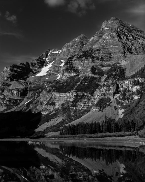 A black and white landscape shows mountains with snow and trees reflected in a lake.