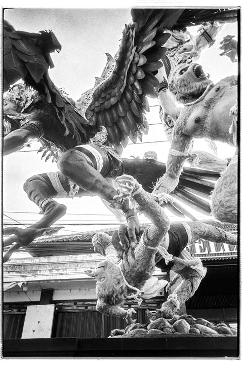 A low-angle, black and white shot captures a dynamic sculpture of winged and monkey-like figures against a bright sky.