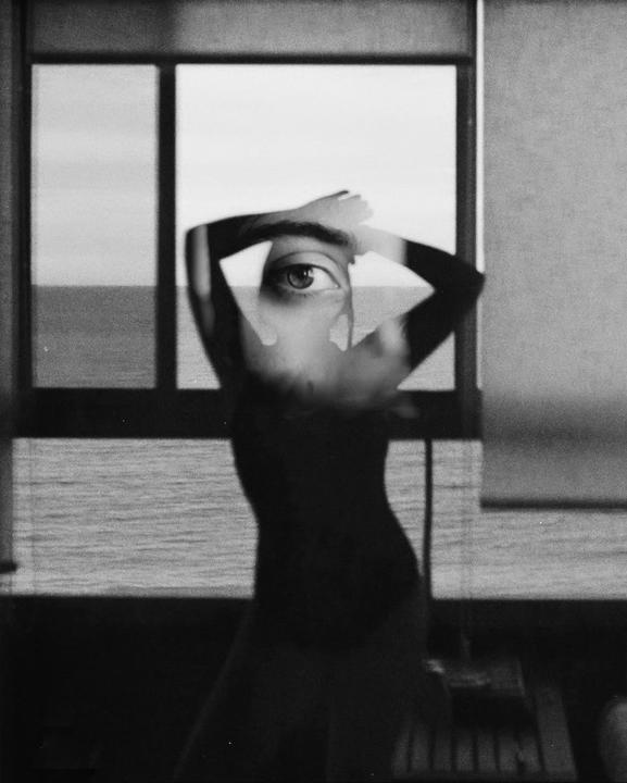 A double exposure shows a woman's silhouette with an eye superimposed over her head, set against a window overlooking the ocean.