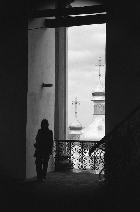 A woman stands on a balcony overlooking church domes with crosses against a cloudy sky.
