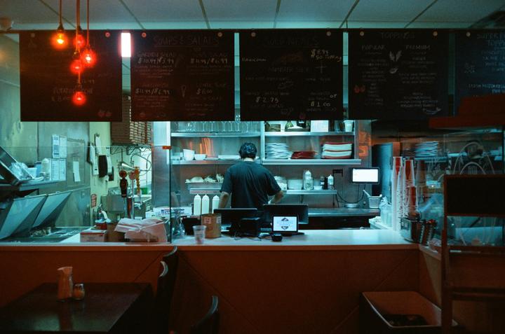 A man works behind a counter in a restaurant kitchen with menus hanging above.