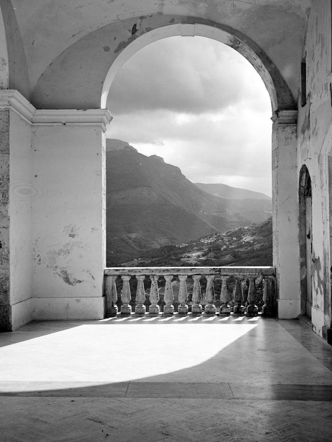 A mountain landscape is visible through an archway and over a stone balustrade.