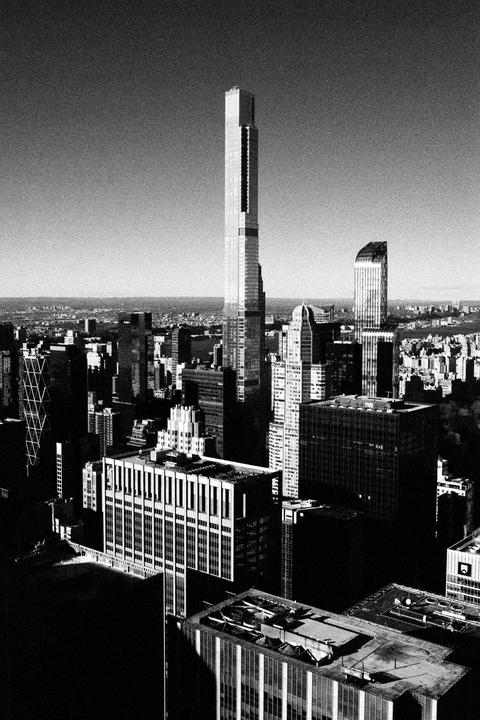 An aerial view shows a dense urban landscape with numerous skyscrapers under a clear sky.