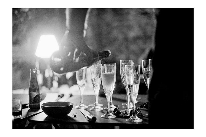 A person pours champagne into a flute glass on a table with other glasses and a bowl.