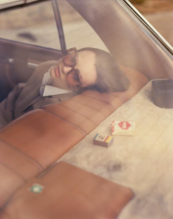 A woman wearing sunglasses is resting in the back seat of a car.