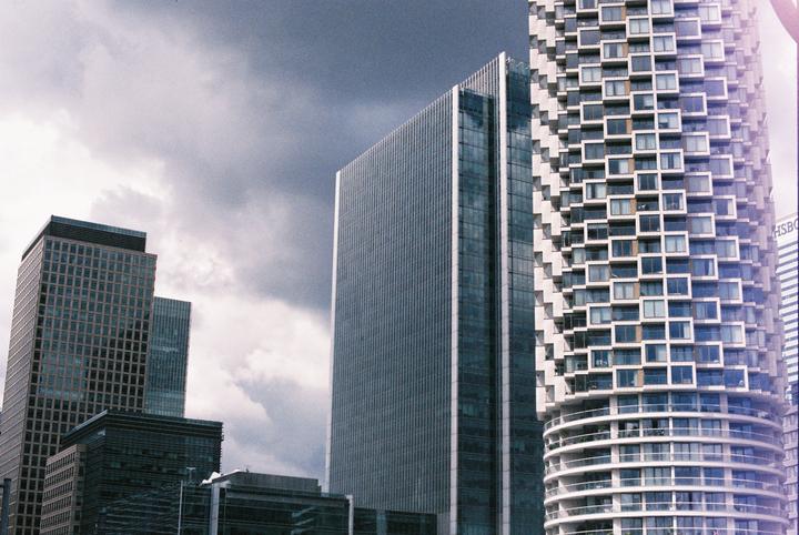 Several tall buildings with varied architectural styles stand against a cloudy sky.