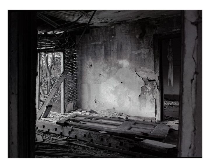 A derelict room with a collapsed ceiling and debris on the floor is illuminated by light from an open doorway.