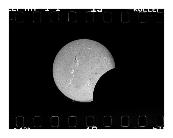 A solar eclipse is visible through a film strip with sprocket holes.