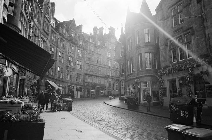 A sun-drenched street with cobblestones and tall buildings is lined with shops and a few people.