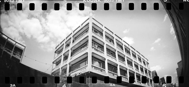 A low-angle, wide-shot captures a brutalist building against a cloudy sky.