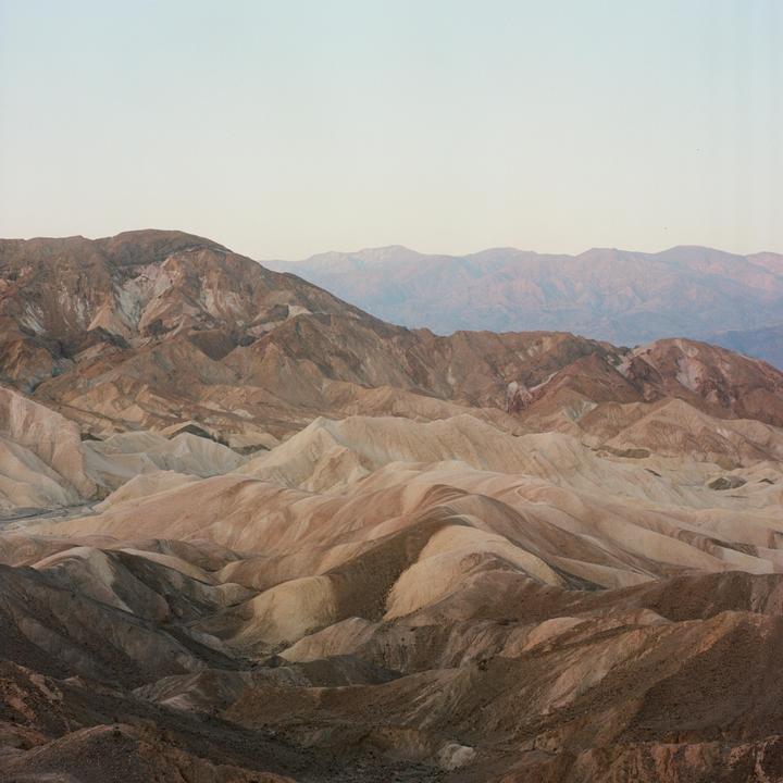 A vast desert landscape features rolling hills and mountains under a pale sky.